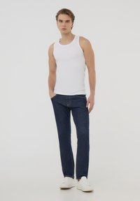 Top bianco senza maniche con scollatura rotonda, abbinato a jeans in denim blu scuro. I jeans hanno una vestibilità dritta con cuciture visibili.