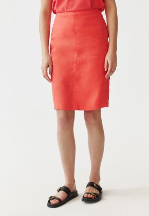 Jupe crayon en lin corail avec taille haute, longueur aux genoux et texture lisse. Associée à des sandales plates noires avec des accents dorés.