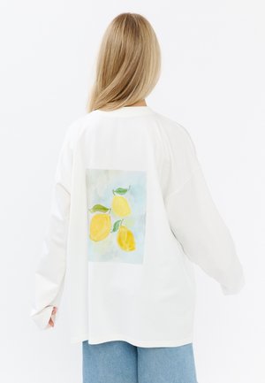Witte long-sleeve shirt met een vierkante, lichtblauwe afdruk van gele citroenen en groene bladeren op de achterkant, ontworpen voor een relaxte pasvorm.