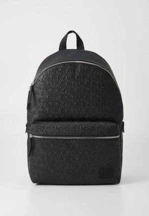 Mochila preta feita de material texturizado, apresentando um padrão de logótipos em relevo. Tem um topo arredondado, bolso frontal com fecho e alças ajustáveis.