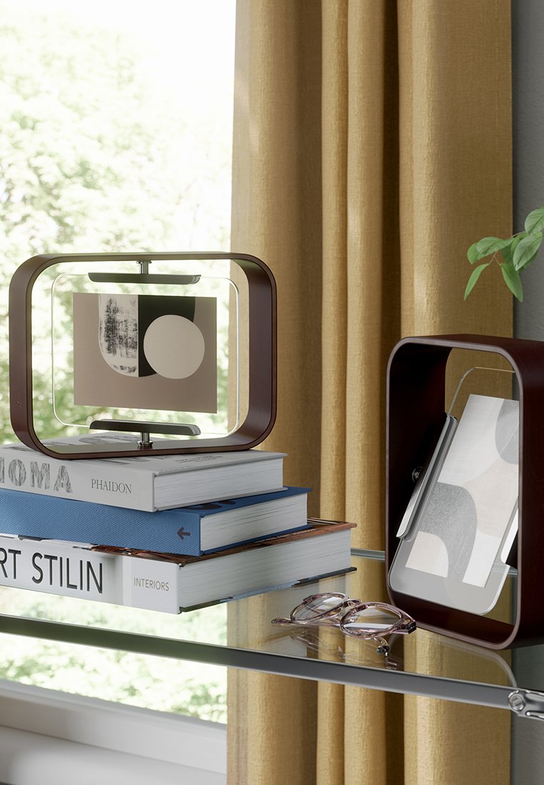 Dwie dekoracyjne ramki w bogatym brązowym wykończeniu, prezentujące sztukę abstrakcyjną, umieszczone na stosie książek z przezroczystą powierzchnią obok nich szklanki.