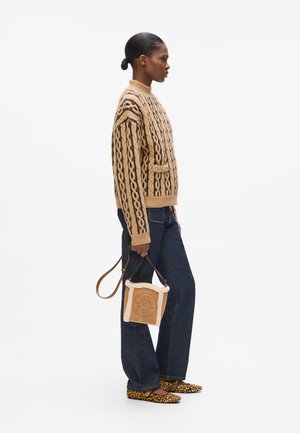 Pull en tricot beige avec des torsades, col montant et poche latérale. Jean ample bleu foncé. Petit sac beige avec un haut en crème doublé. Chaussures imprimé léopard.