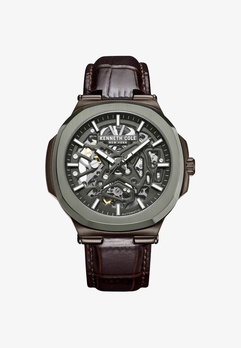 Automatisch horloge met een bruine leren band, grijze skeleton wijzerplaat, metalen accenten en een gedurfde octagonale kast met zichtbare mechanismen.