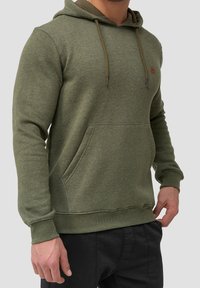 Sudadera verde oliva con un bolsillo frontal, cordón ajustable y puños acanalados. Presenta un pequeño logo en el pecho, fabricada con una tela suave.