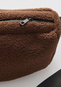 Pochette in pile marrone con zip nera e tracolla su sfondo bianco.