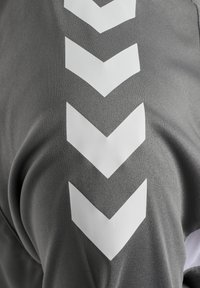 Tissu gris avec cinq grandes flèches blanches en forme de chevrons pointant vers le bas, disposées verticalement.