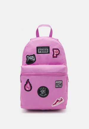 Roze rugzak met Puma-logo's, patches van een panterkop, letter P, vlam, basketbalbadge en sneaker. Voorvak met ritssluiting en bovenhandvat.