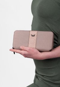 Beige wallet with a woven pink stripe, featuring a black logo and zip closure. Material appears textured and durable, held in a hand.