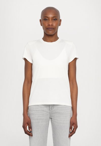 T-shirt blanc à manches courtes avec un col rond, en tissu lisse, au design ajusté et à la texture subtile. Associé à un jean gris clair.