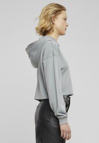 Felpa grigia chiara tagliata con cappuccio regolabile, polsini a coste e vestibilità rilassata, abbinata a pantaloni in pelle nera attillati.