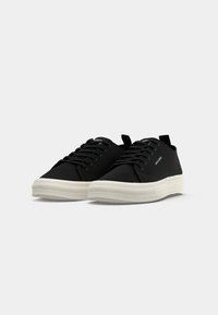 Ein Paar schwarze Low-Top-Sneaker mit weißen Gummisohlen und Schnürsenkeln, nebeneinander auf einem schlichten hellen Hintergrund platziert.