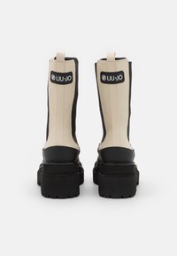 Botines de cuero en beige y negro con suelas gruesas negras, vistos desde la parte trasera, con etiquetas de la marca Liu Jo en la zona superior del tacón.