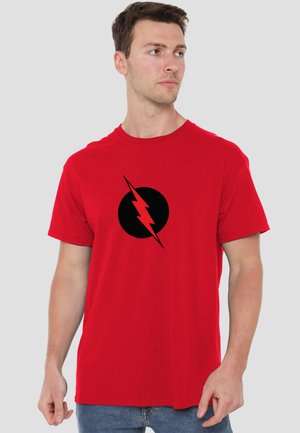 Young man wearing a red t-shirt with a black circle and red lightning bolt design, looking to his left against a plain background.