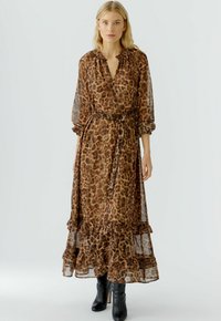 Maxi-jurk met luipaardprint in doorzichtig bruin materiaal, voorzien van ruches aan de mouwen en zoom. Heeft een strikceintuur en een enkellange snit, gecombineerd met zwarte laarzen.