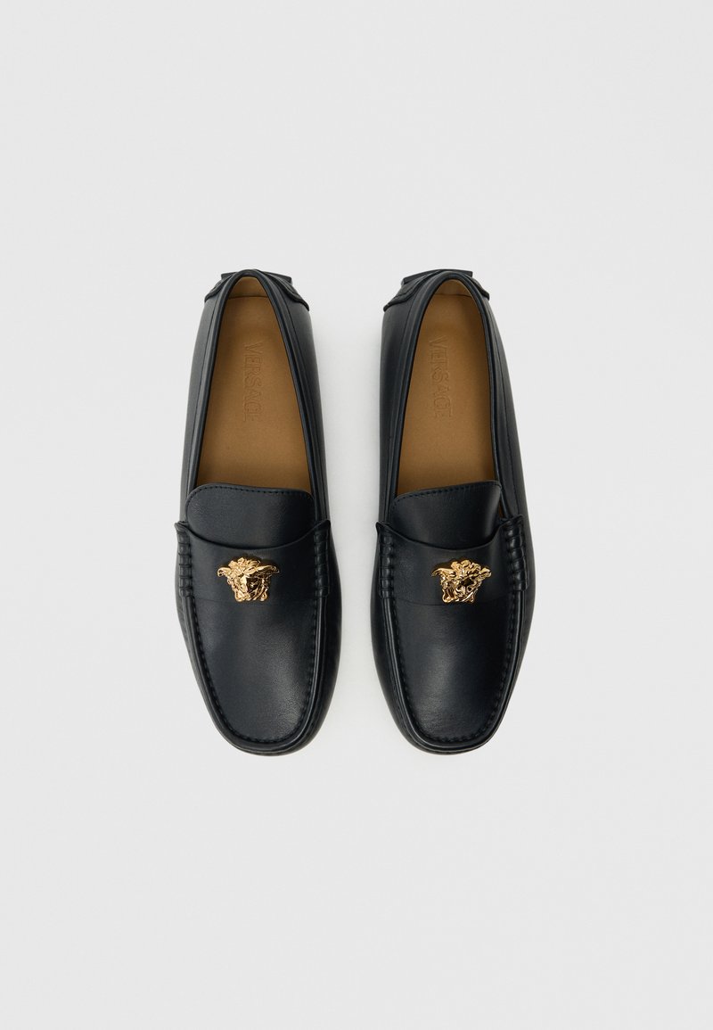 Schwarze Lederloafers mit einem goldenen Akzent in Form eines Löwenmotivs, handgenähte Details und eine glatte Oberfläche. Formelles Design mit abgerundeter Form.