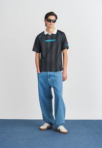 Jersey da Reebok com listras pretas e detalhes em azul, combinado com jeans largos azul claro e ténis brancos.