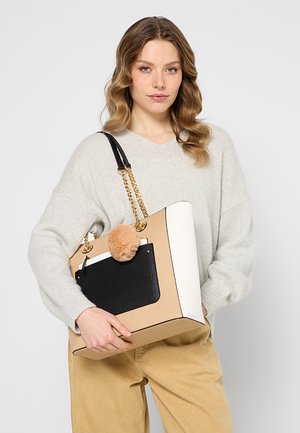 Beige og hvid struktureret håndtaske med en sort lomme og en tan pom-pom charm, der har guld hardware og en kædestrop.