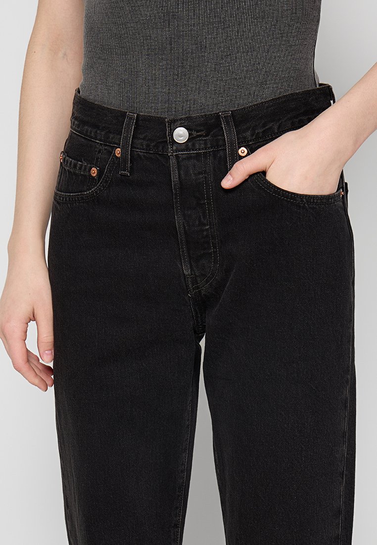 Jeans de mezclilla negra con un diseño de cintura alta, cinco bolsillos y herrajes en tono cobre. Terminado con un cierre de cremallera y botón.