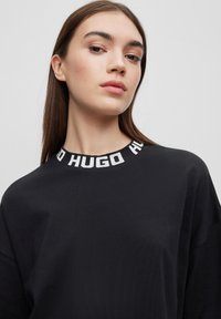 Felpa nera con texture a costine, caratterizzata da un collo rotondo decorato con il logo bianco "HUGO". Vestibilità ampia con maniche lunghe.