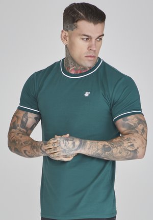 Tamnozeleni majica kratkih rukava s bijelim obrubom oko ovratnika i rukava. Sadrži mali logo na prsima. Mekani teksturni materijal.