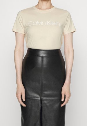 Woman wearing beige Calvin Klein t-shirt tucked into a high-waisted black leather pencil skirt with front slit and seam details.