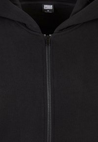 Sweat à capuche noir zippé avec fermeture éclair visible et étiquette à l'intérieur du col indiquant Urban Classics, taille medium, fabriqué en Chine.