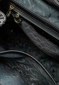 Interno della borsa con tessuto testurizzato verde scuro caratterizzato da un sottile motivo a spirale. Cerniera nera e accenti in oro visibili.