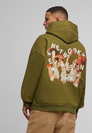 Olivengrønt hætte sweatshirt med svampegrafik og fed hvid tekst der siger "NETWORK EXPANSION PACK" på ryggen.