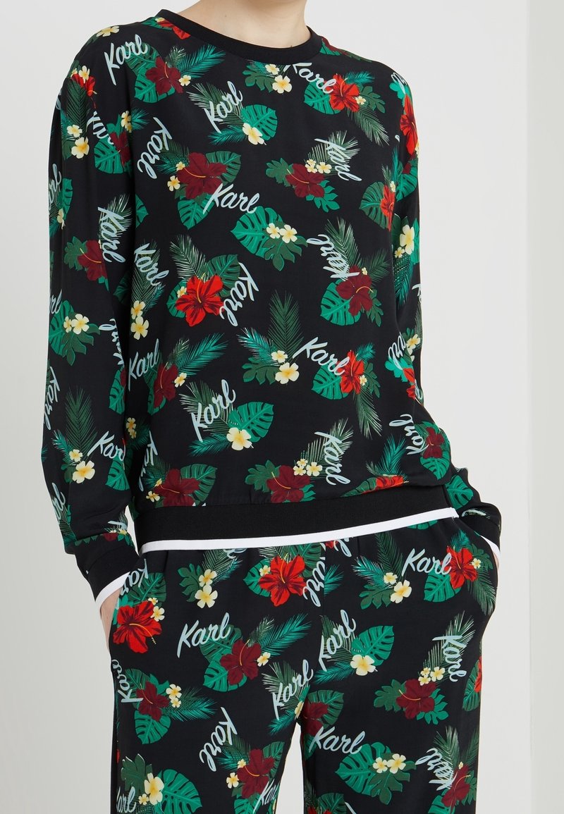 Ensemble sweat-shirt et pantalon noirs avec un motif floral composé de fleurs rouges et jaunes et de feuilles vertes, agrémenté du nom "Karl" en texte blanc.
