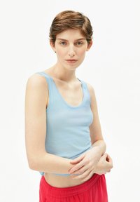 Hellblaues Tanktop mit rundem Ausschnitt, figurbetontem Schnitt und glatter Textur. Kombiniert mit roten Jogginghosen, die ein lässiges Outfit zeigen.