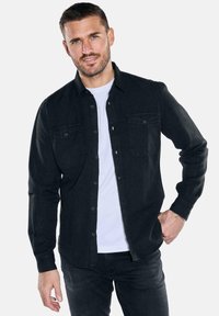 Schwarzes Hemd mit Knöpfen aus einem glatten Stoff, ausgestattet mit zwei Brusttaschen und einem klassischen Kragen, kombiniert mit einem weißen T-Shirt darunter.