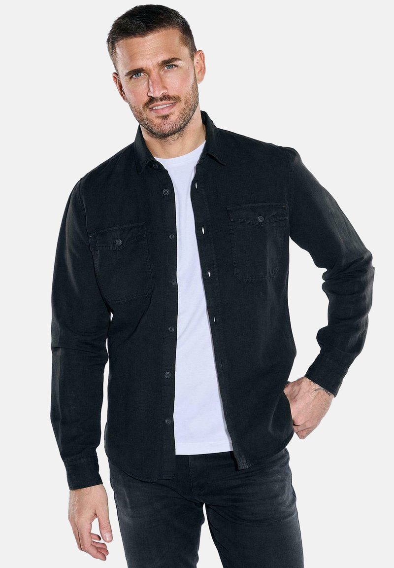 Schwarzes Hemd mit Knöpfen aus einem glatten Stoff, ausgestattet mit zwei Brusttaschen und einem klassischen Kragen, kombiniert mit einem weißen T-Shirt darunter.