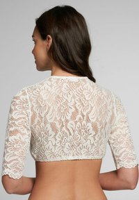 Spitzen-Crop-Top mit kurzen Ärmeln, ausgestattet mit einem Blumenmuster und gewellten Kanten. Das Material ist durchsichtig und in einer cremigen Farbe.