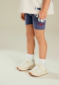 Blaue Shorts mit "TEAM GB" in Rot, weiße Sportschuhe und weiße Socken, mit strukturierten Einsätzen und einem Riemenverschluss.