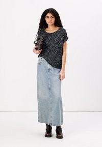 Black leopard print short-sleeve top, light blue denim maxi skirt, and ankle-height black leather boots, holding a dark handbag.