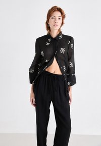 Chemise noire à boutons avec des motifs de feuilles brodés en blanc contrastant, dotée de manches longues et d'une coupe décontractée, associée à un pantalon noir à cordon de serrage.