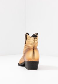Golden ankle boot with textured snake-skin pattern, black interior, and a low wooden heel. Smooth metallic finish on the back.