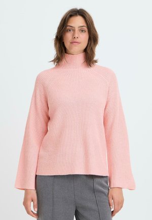 Rosa gestrickter Rollkragenpullover mit lockerem Schnitt, weiten Ärmeln und geripptem Muster. Kombiniert mit grauen Hosen.
