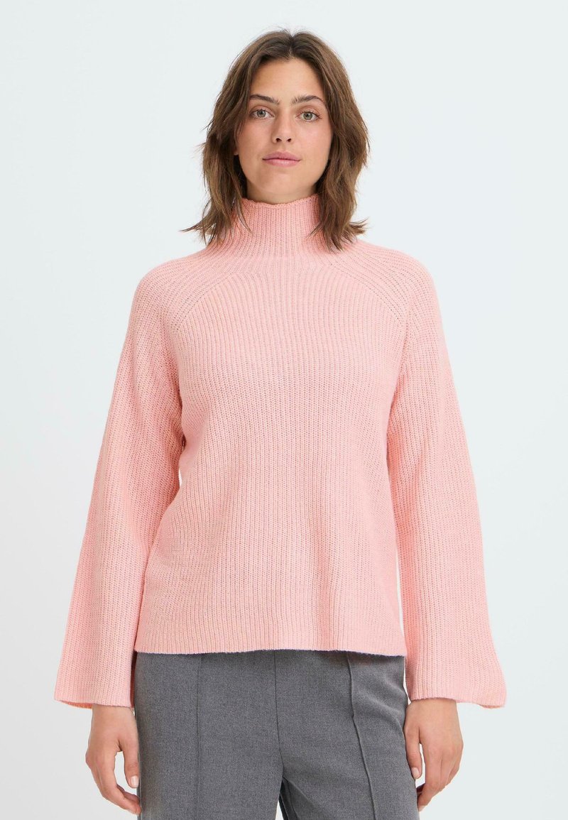 Maglione a collo alto rosa lavorato a maglia, con vestibilità comoda, maniche ampie e texture a coste. Abbinato a pantaloni grigi.