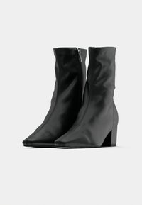 Ζεύγος μαύρων μποτών αστραγάλου με τακούνια block και πλαϊνά φερμουάρ, με λείο δερμάτινο φινίρισμα και μυτερές μύτες.