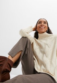 Maglione di cotone color crema a maglia cables con colletto alto, abbinato a pantaloni a disegno houndstooth marroni e stivaletti alla caviglia in suede marroni.