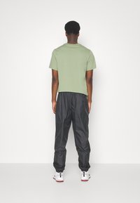 Grön bomullströja och svarta, lätta byxor med elastisk midja. Skorna har vitt med röda accenter. Minimalistisk design utan logotyper.