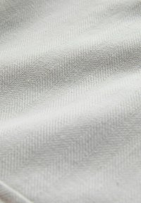 Gros plan d’un tissu doux gris clair présentant un fin motif en chevrons avec des plis légers et des détails de texture.