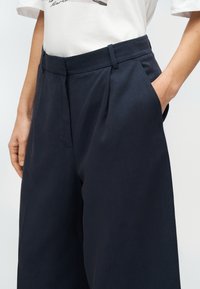 Ναυτικά παντελόνια με φαρδιά παντελόνα, με πιέτες μπροστά, λείο υλικό και πλαϊνές τσέπες. Διαθέτει εφαρμοστό ζωνάκι και καθαρές γραμμές.