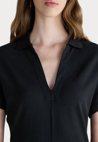 T-shirt noir de style polo à manches courtes, avec un décolleté en V et un tissu texturé. Détails de coutures visibles sur le devant.