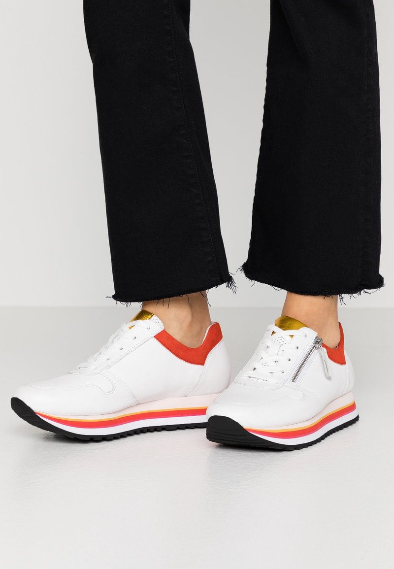 Baskets en cuir blanc avec accents rouges, détails dorés et semelles rayées multicolores ; lacets et fermeture éclair latérale ; matière texturée.