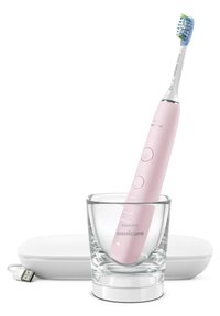 Brosse à dents électrique avec un manche rose dans un verre. Elle dispose de deux boutons et d'une tête de poils bleus et verts. Comprend un étui de chargement blanc.