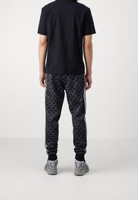 Czarny t-shirt z krótkim rękawem w połączeniu z czarnymi, teksturowanymi spodniami dresowymi z wzorem ptaków i białymi bocznymi paskami. Szare sneakersy dopełniają strój.