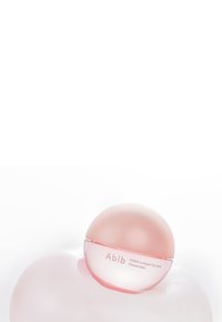 Masque à lèvres en collagène Abib PDRN dans un contenant sphérique, avec un extérieur rose brillant, une base transparente et une texture lisse.
