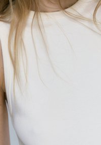 Helles beiges, ärmelloses Top mit glatter Textur und einfachem Ausschnitt, ohne sichtbare Muster oder Verzierungen.